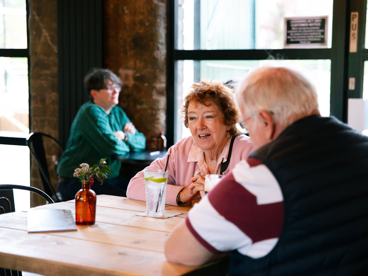 An older woman and man talking across a table in a cafe.